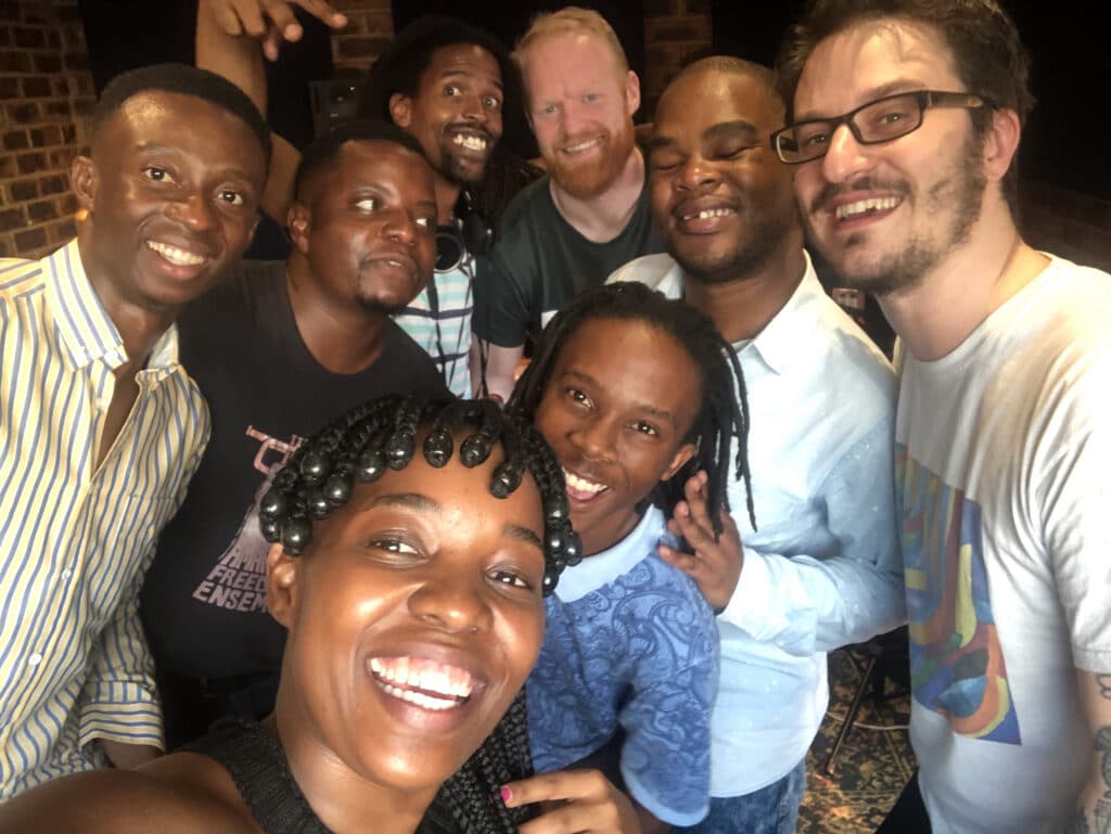 The Equal Spirits band, a group of 8 musicians, smile at the camera in a group selfie.