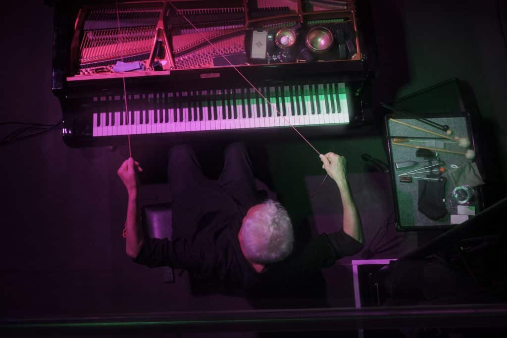 Aerial shot of Heiner Goebbels manipulating long strings pulled attached to the inside of the piano.