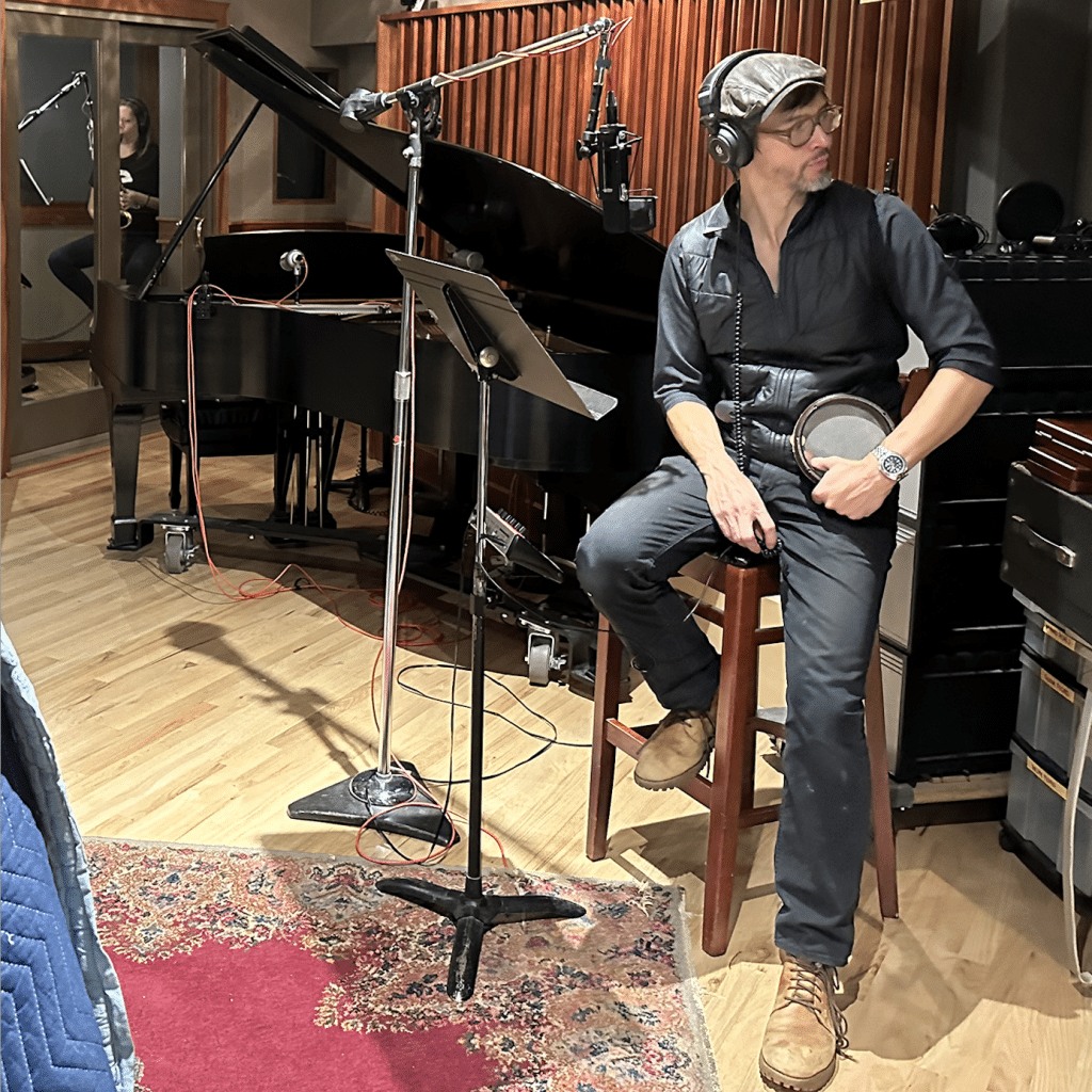 Miles Okazaki sits in the recording studio in front of a music stand and a mic.