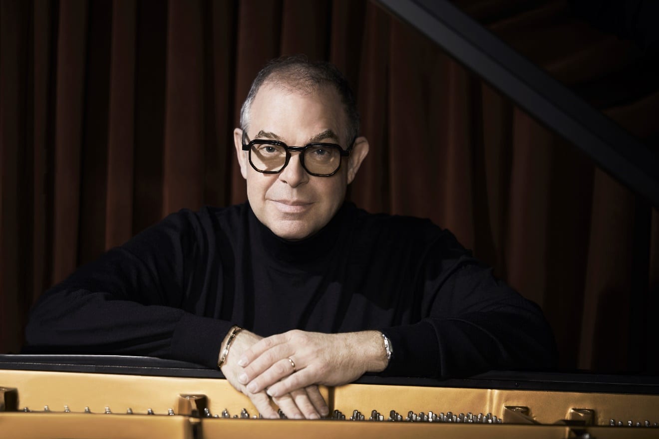 Bill Charlap looks directly into the camera across the open lid of a piano.