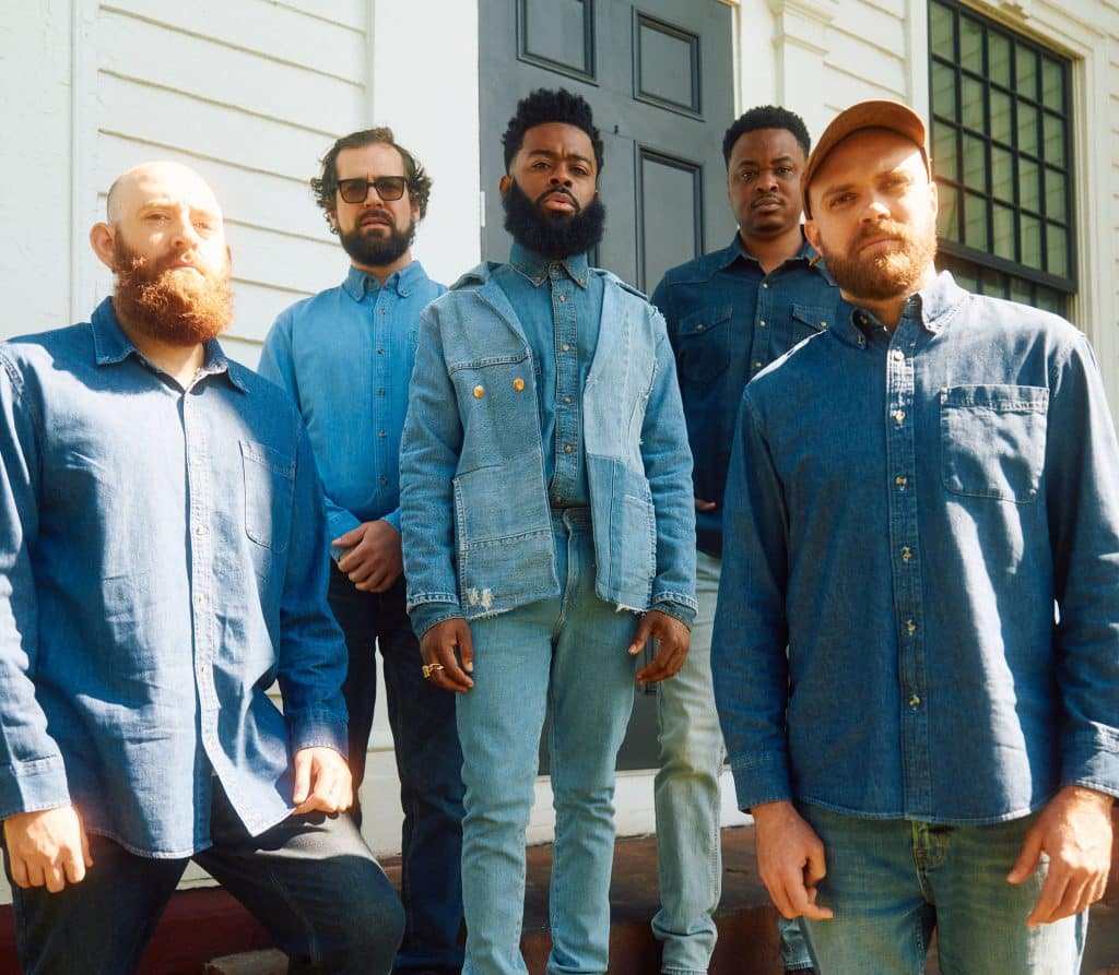 The five members of Vision ahead stand outside in the sun, all wearing denim and looking directly into the camera with serious expressions.