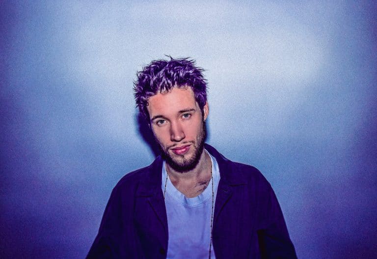 Simon Moullier stands against a blue background, looking directly into the camera.