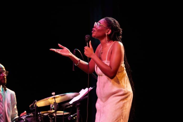 Ekep Nkwelle stands on stage, reaching out a hand. Her face is full of expression as she sings.